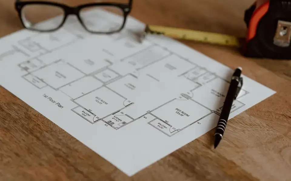Planta de um imóvel sobre a mesa, com trena, caneta e óculos ao lado